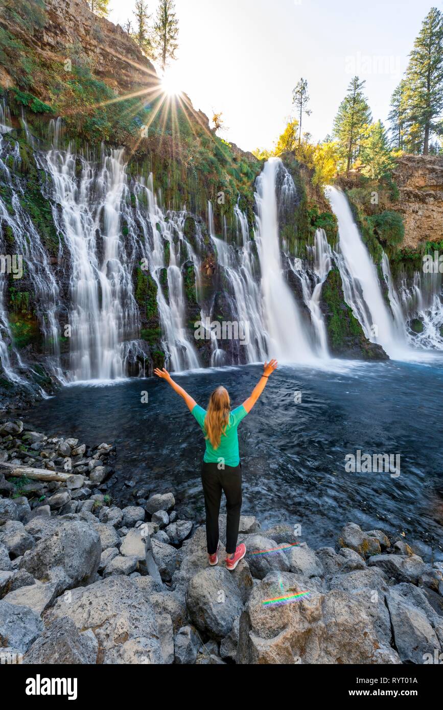 Jeune femme debout dans une chute, s'étirant les bras en l'air, McArthur-Burney Falls Memorial State Park, Californie, USA Banque D'Images