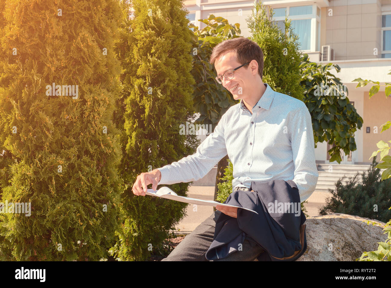 Jeune homme d'affaires dans les verres se lit les documents et les sourires dans la rue. le mec est tenue de l'enveloppe dans ses mains. tonique Banque D'Images