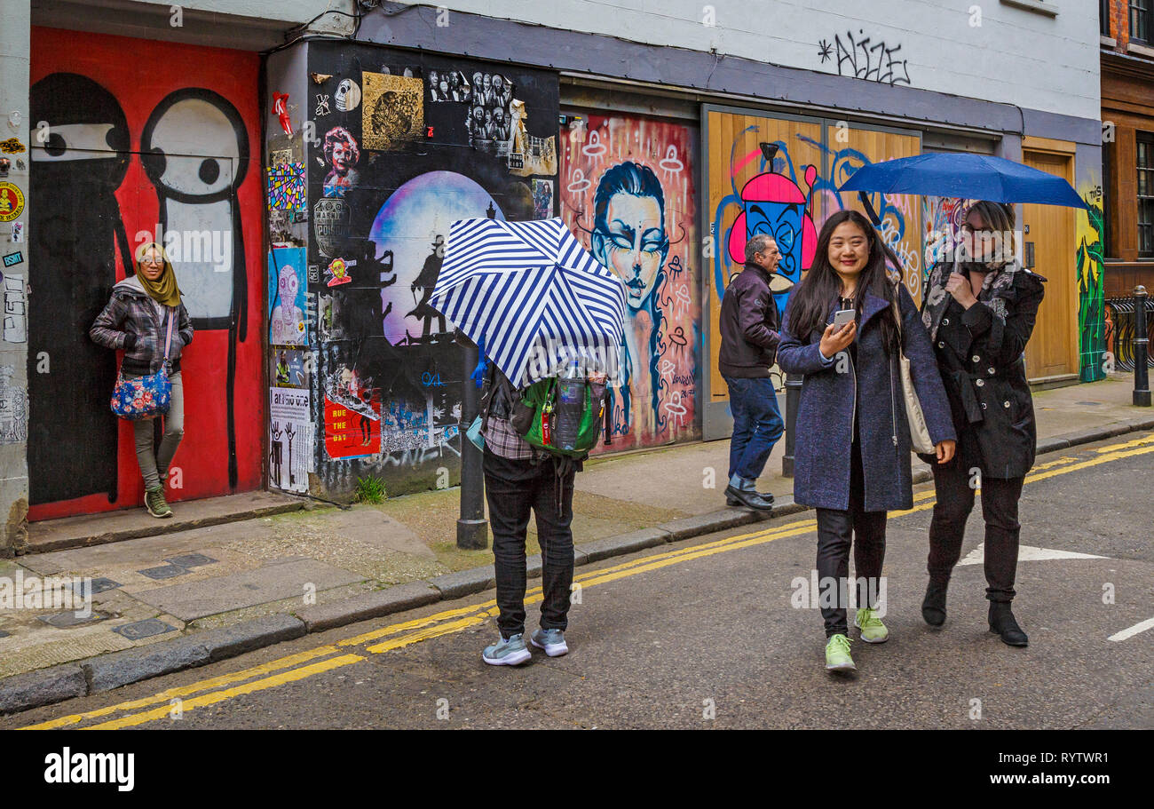 Un groupe de touristes sont représentées autour des graffiti populaires quartiers de l'East End londonien, au Royaume-Uni. Banque D'Images