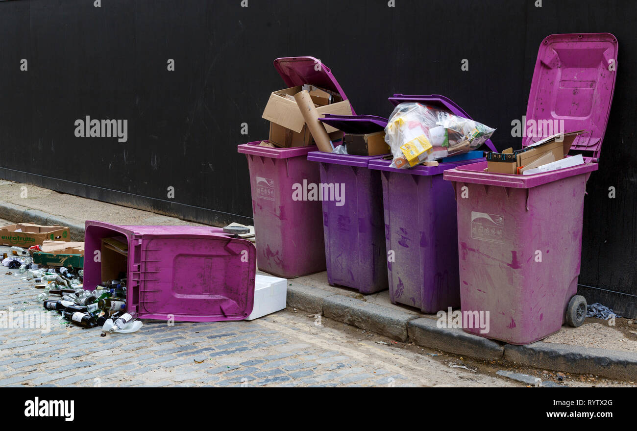 Violet et rose poubelles déborder et les bouteilles de verre sur le sol d'une case sur le côté. Banque D'Images