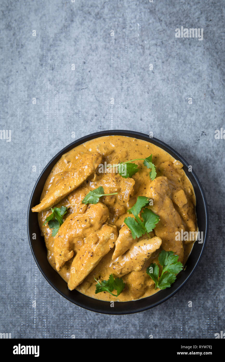 Poulet korma curry au centre dans un bol noir et fond gris clair. Cuvette ronde de poulet korma curry Indien avec des feuilles de coriandre fraîches. Banque D'Images