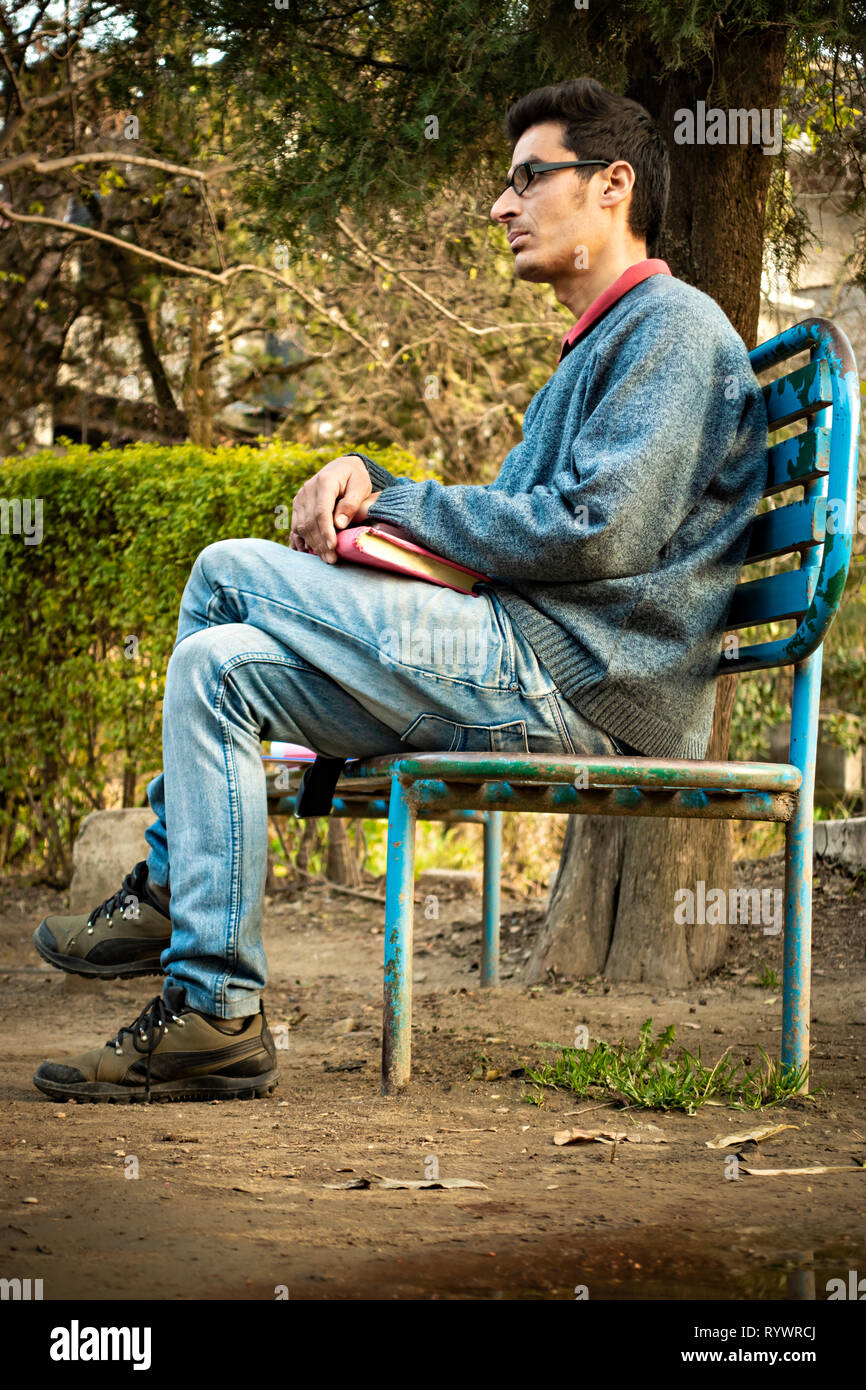 Image extérieur de pays asiatiques, jeunes adultes sereine indien businessman sitting on park bench, holding business planner et de penser tout en regardant loin à voir Banque D'Images
