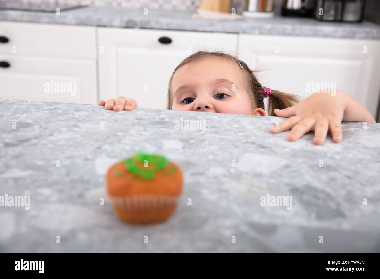 Smiling cute girl looking at Cupcake sur compteur de cuisine Banque D'Images