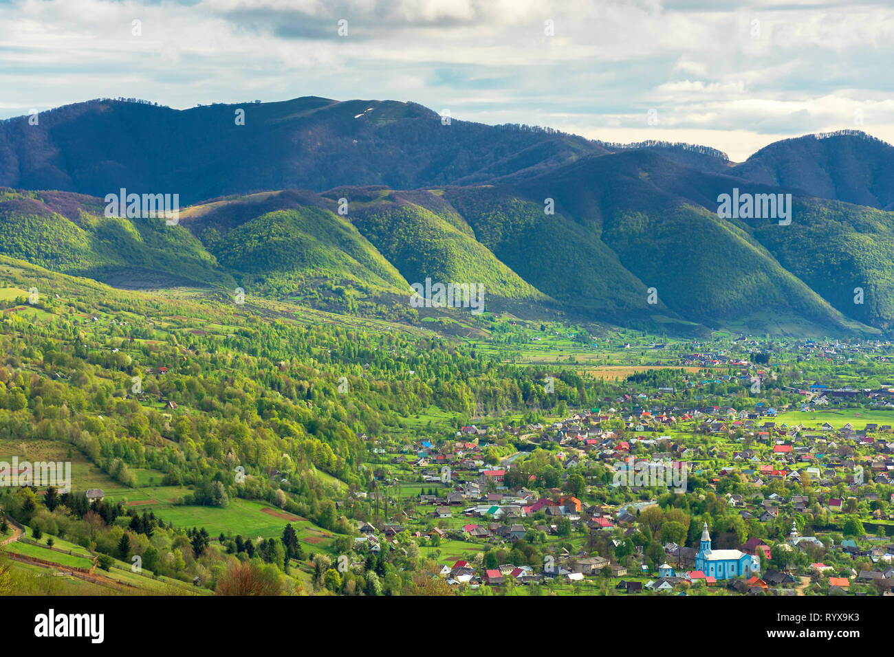 Paysages montagneux au printemps. Village de la vallée, crête de montagne avec des taches de neige. beau temps avec ciel nuageux. vue depuis la colline. Banque D'Images