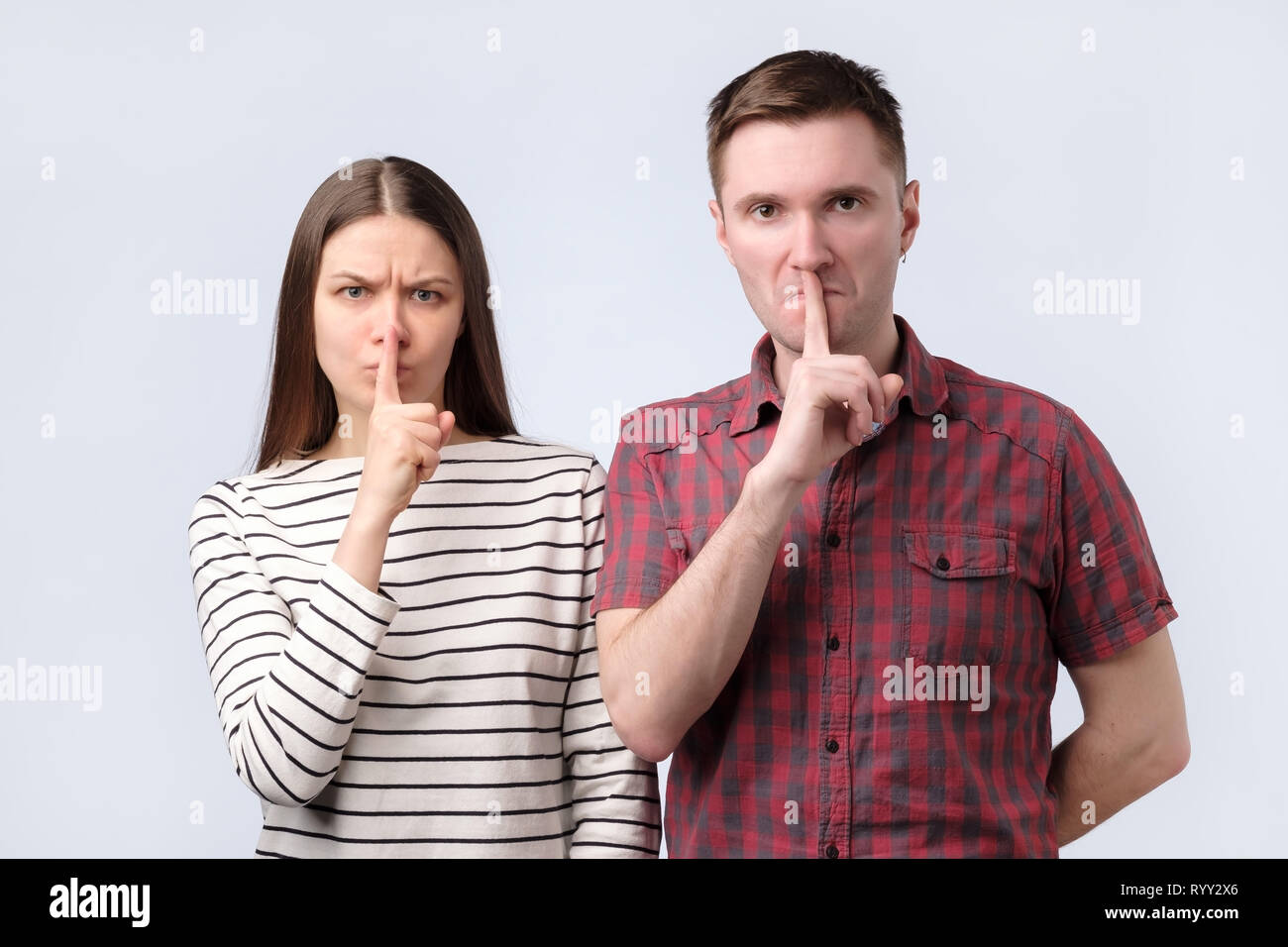 Jeune couple montrant un signe de silence mise en doigt geste bouche sur fond blanc Banque D'Images