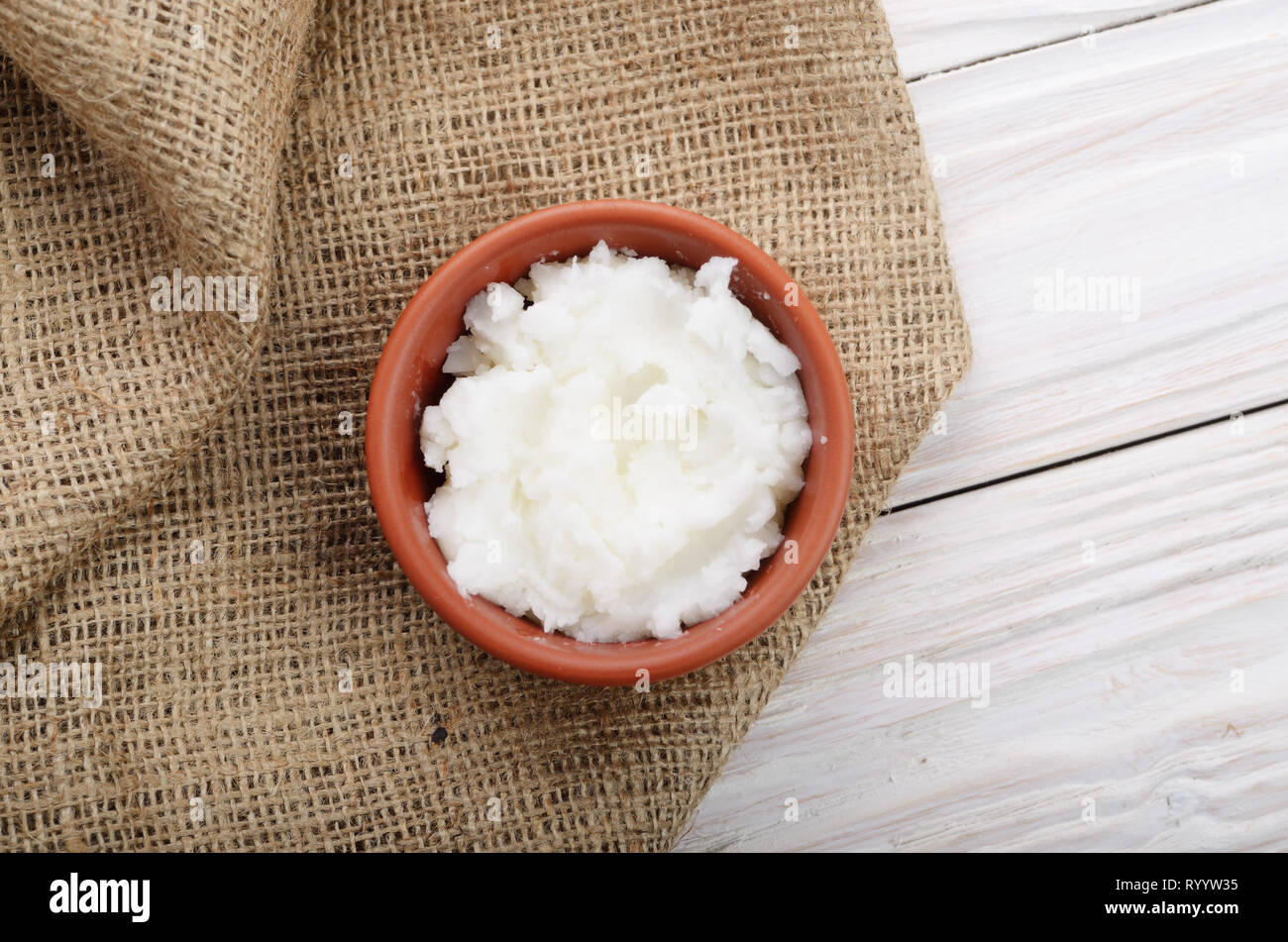 Mise à plat de l'huile de noix de coco dans un bol d'argile brun sur le chanvre sacs sur une table de cuisine en bois blanc Banque D'Images