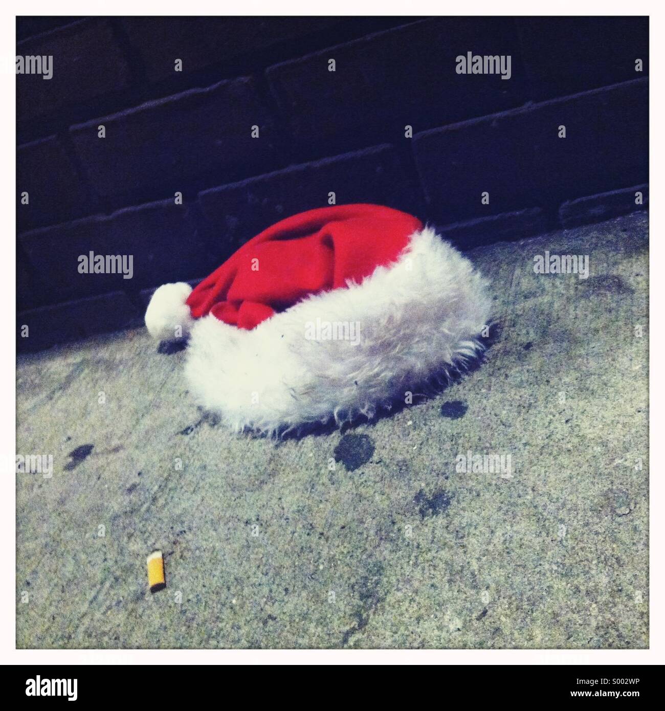 Un rouge et blanc Santa's hat sur un trottoir sale Banque D'Images