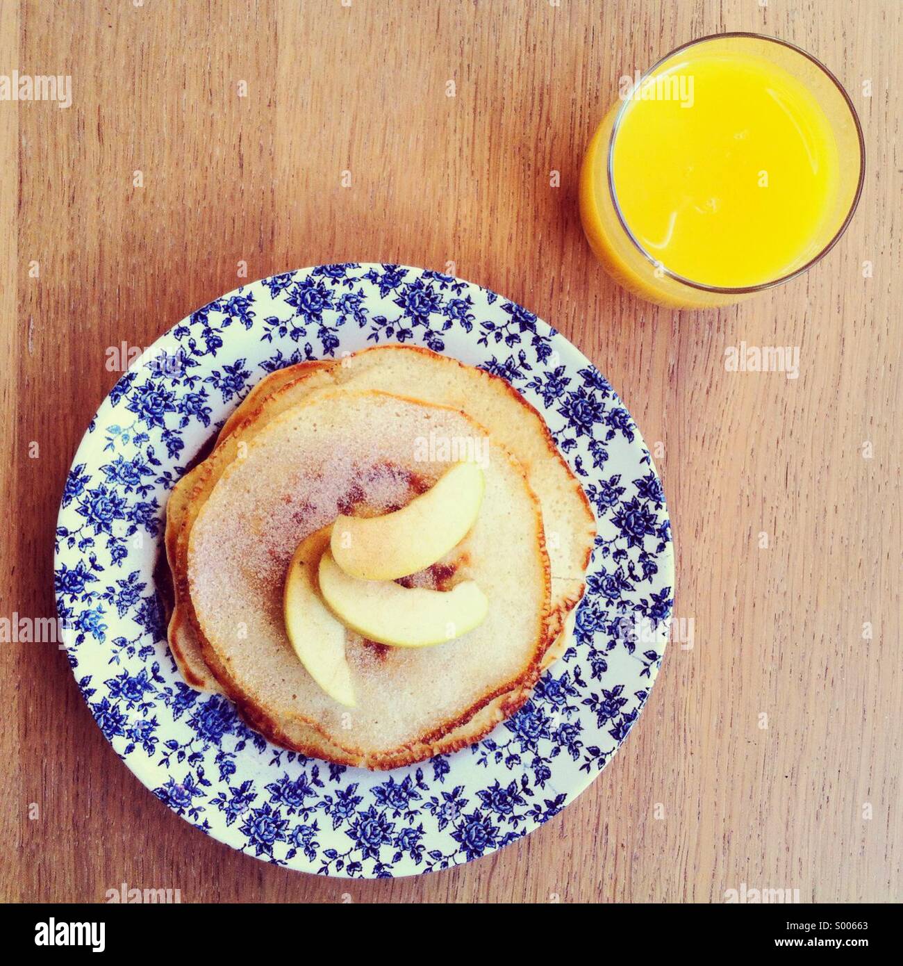 Pile de crêpes américaines garnie de tranches de pommes sur une plaque d'époque, avec un verre de jus d'orange - Image de stock capturée avec un smartphone