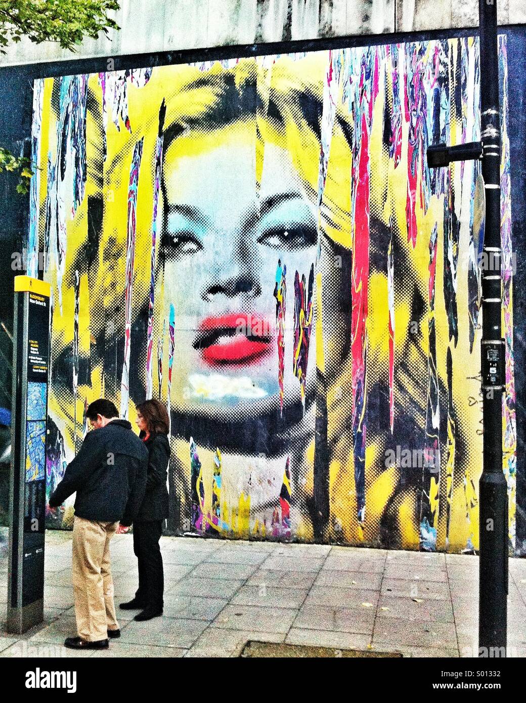 Un couple sont éclipsées par une pâte de Kate Moss, de modèle par artiste de rue, Mr Brainwash (Thierry Guetta). Le travail a été collé à l'extérieur de l'ancien bureau de tri dans le cadre de l'artiste solo show. Banque D'Images