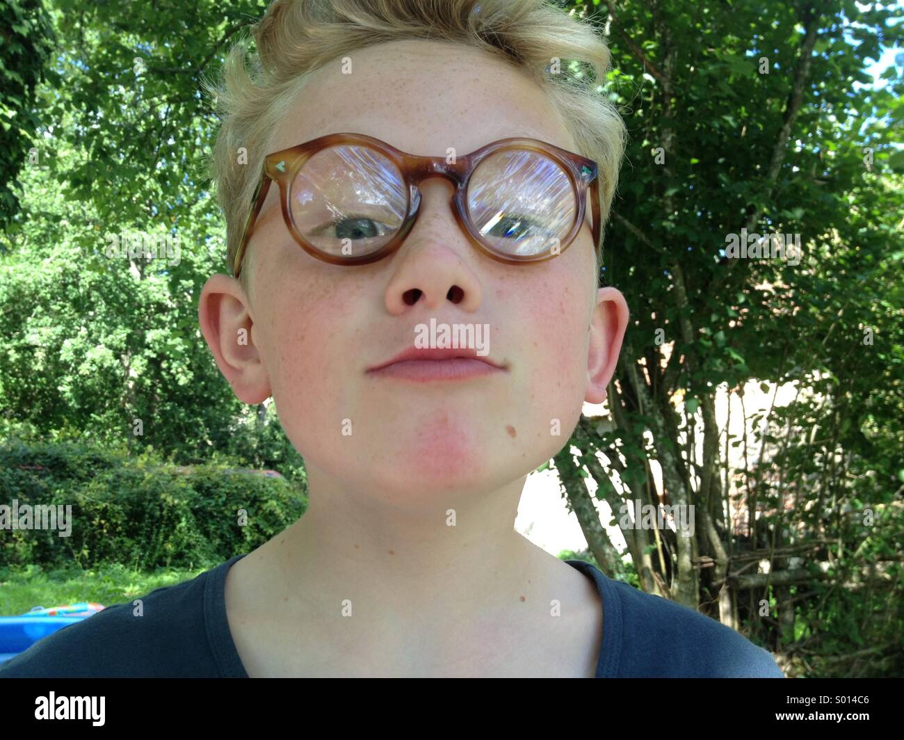 Jeune garçon avec de grandes lunettes rondes, dans un jardin Banque D'Images