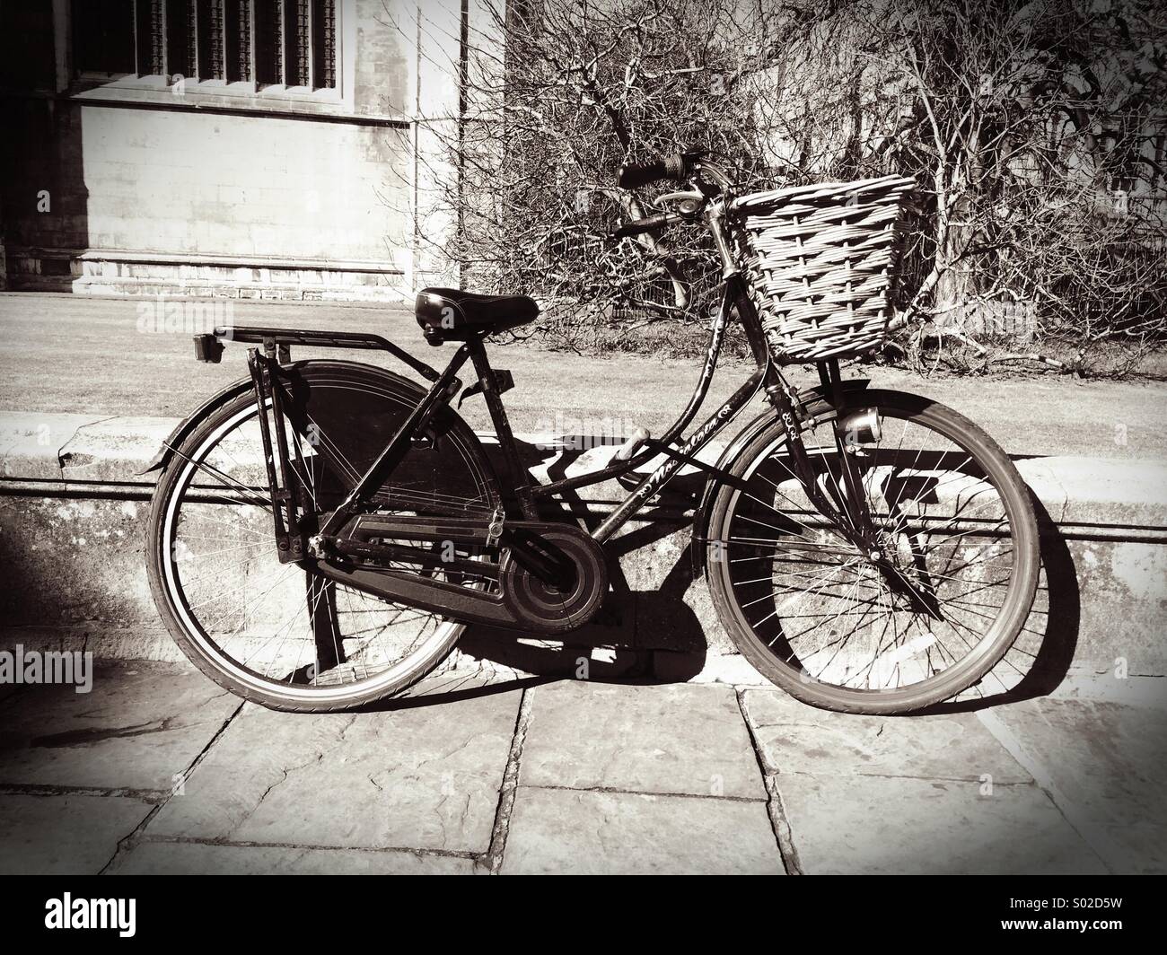 Une pédale avec cycle traditionnel panier appuyé contre un mur à Cambridge UK vintage avec filtre noir et blanc Banque D'Images