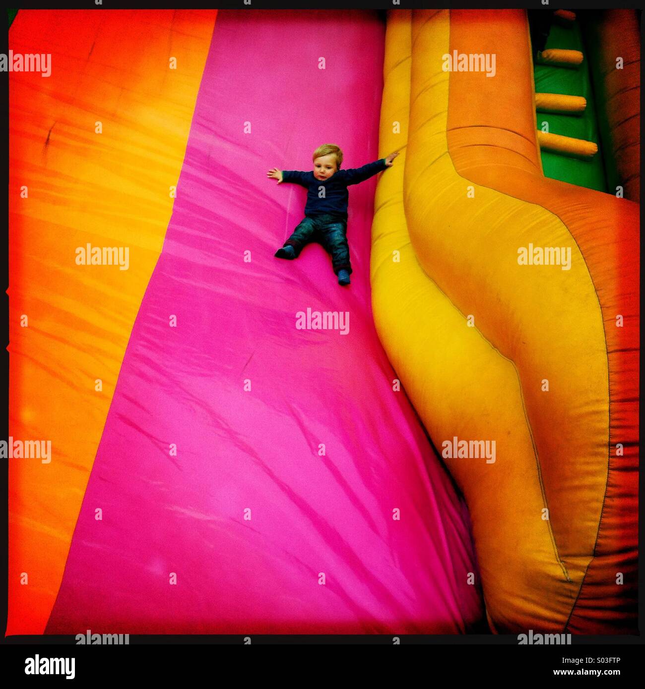 Un jeune garçon de deux ans faisant glisser vers le bas à une diapositive gonflable but fun fair. L'enfant est montrant un certain degré de peur. Banque D'Images