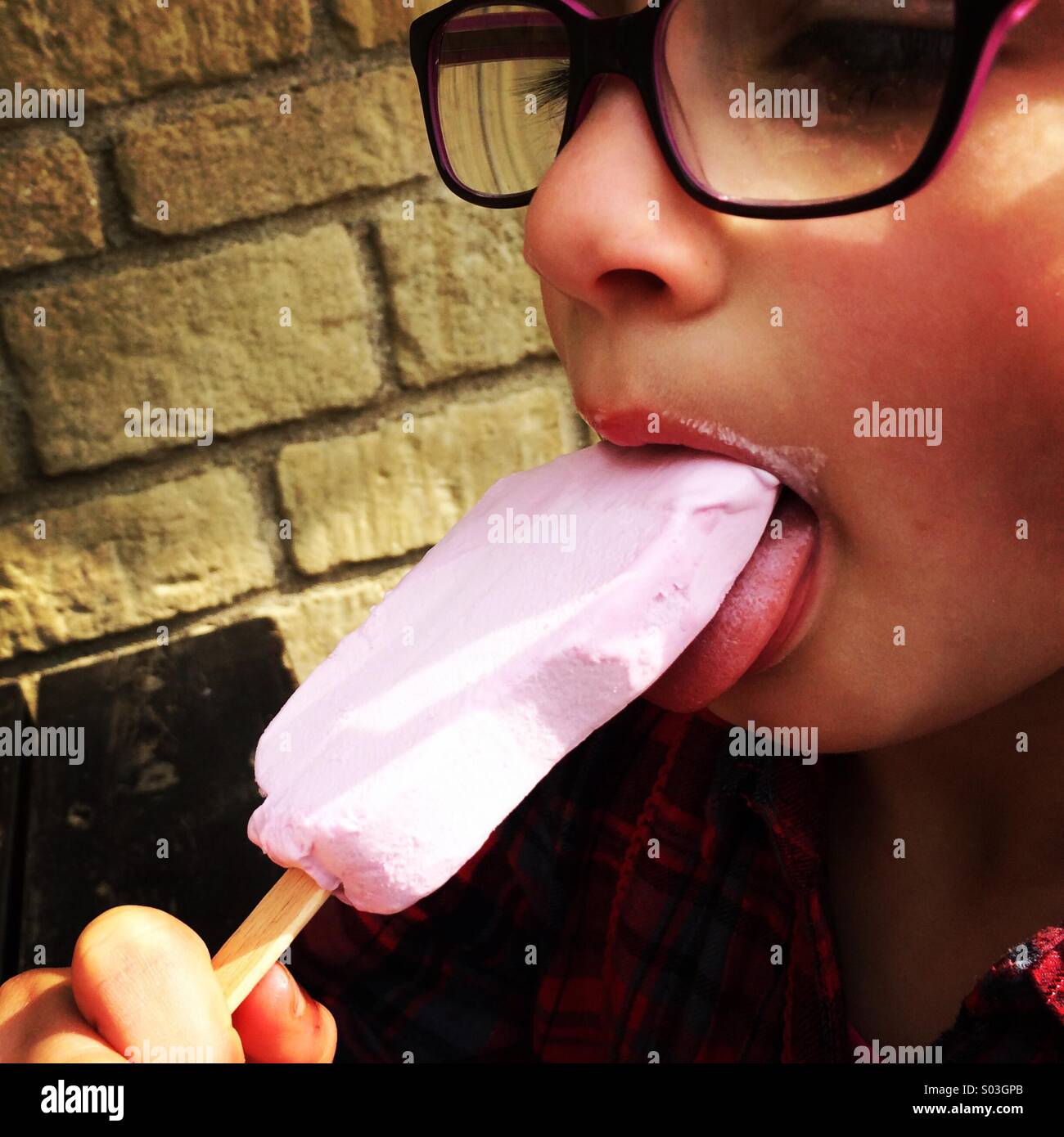 Petite fille portant des lunettes mangeant une glace rose lolly. Banque D'Images