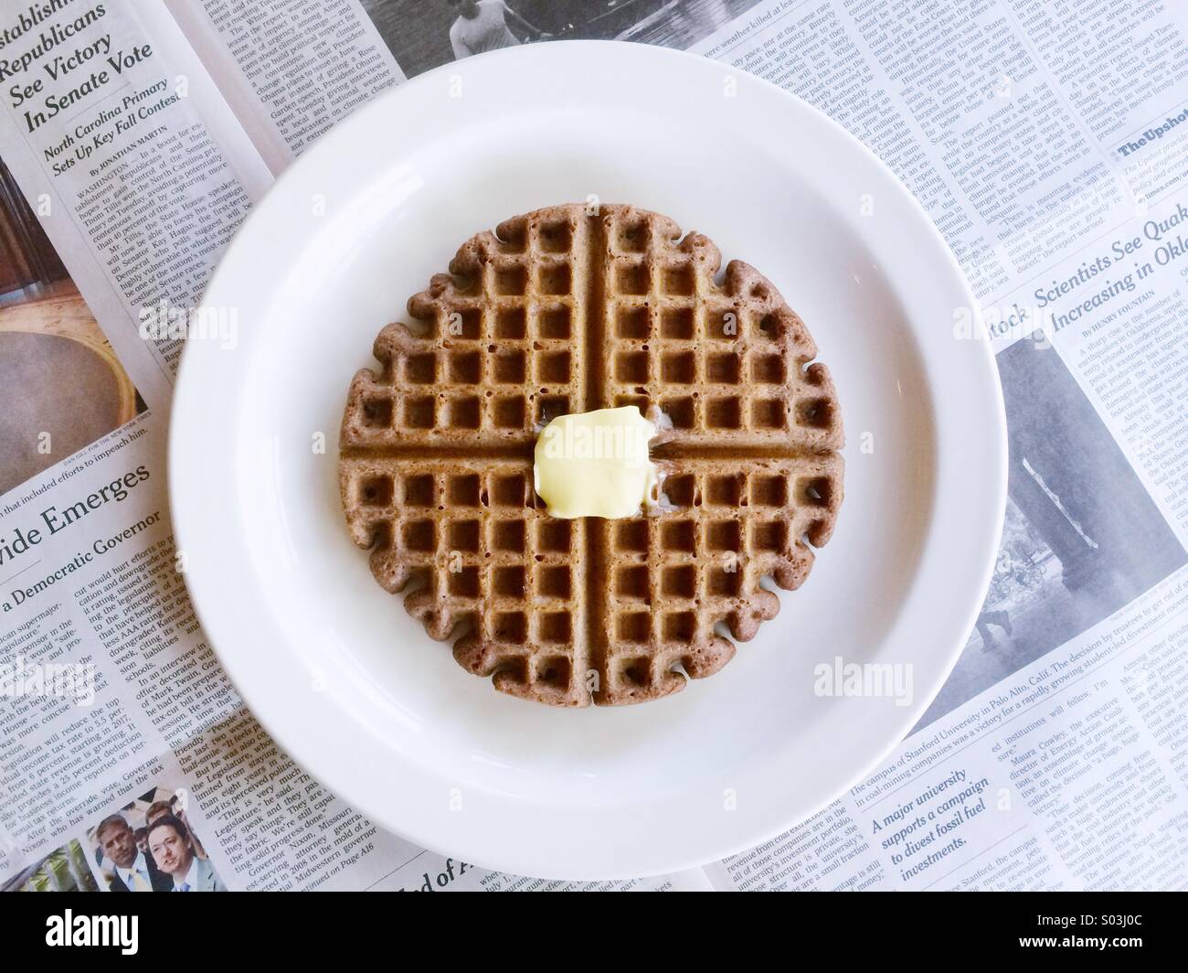 Une gaufre sans gluten pour le petit déjeuner, sur une plaque avec une noisette de beurre et les journaux du matin. Banque D'Images