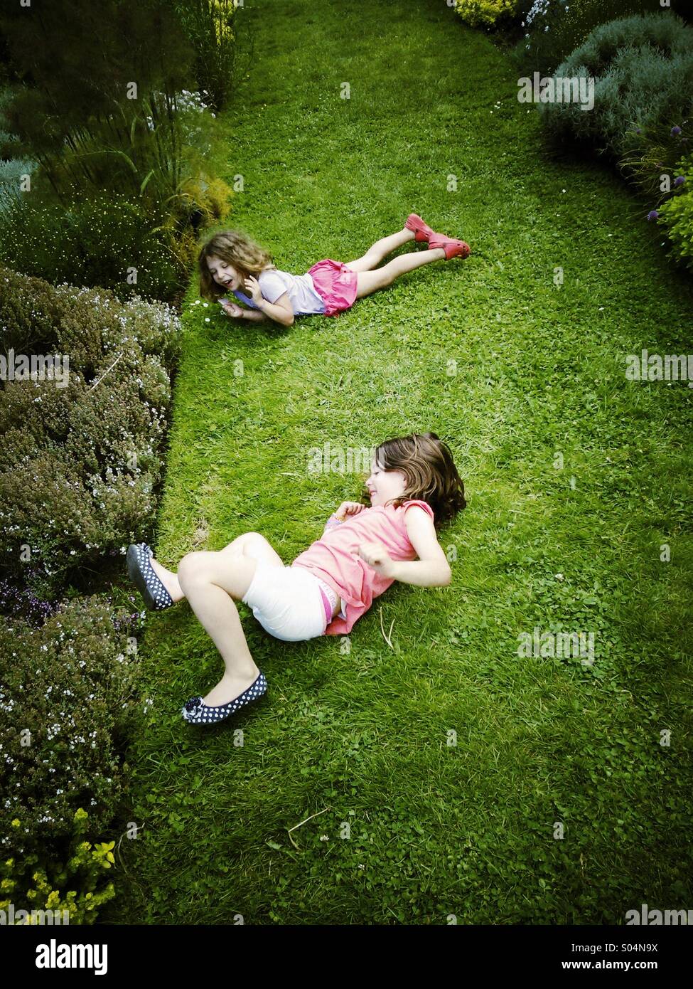 De jeunes enfants jouant roulant sur l'herbe dans le jardin formel. Banque D'Images