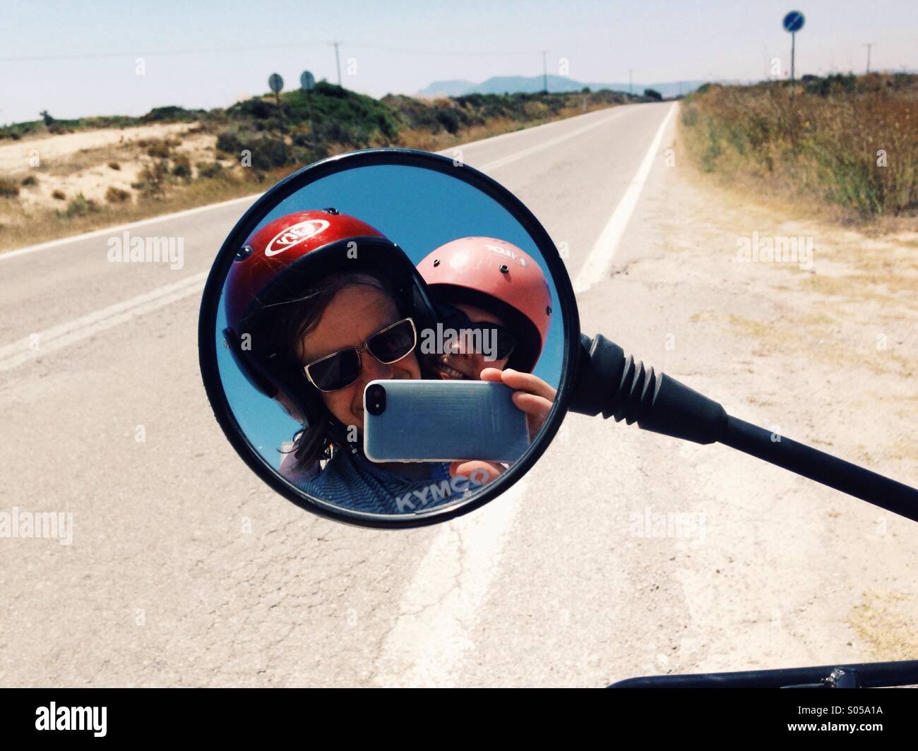 Couple portant des casques de moto dans un miroir avec une route dans l'arrière-plan Banque D'Images