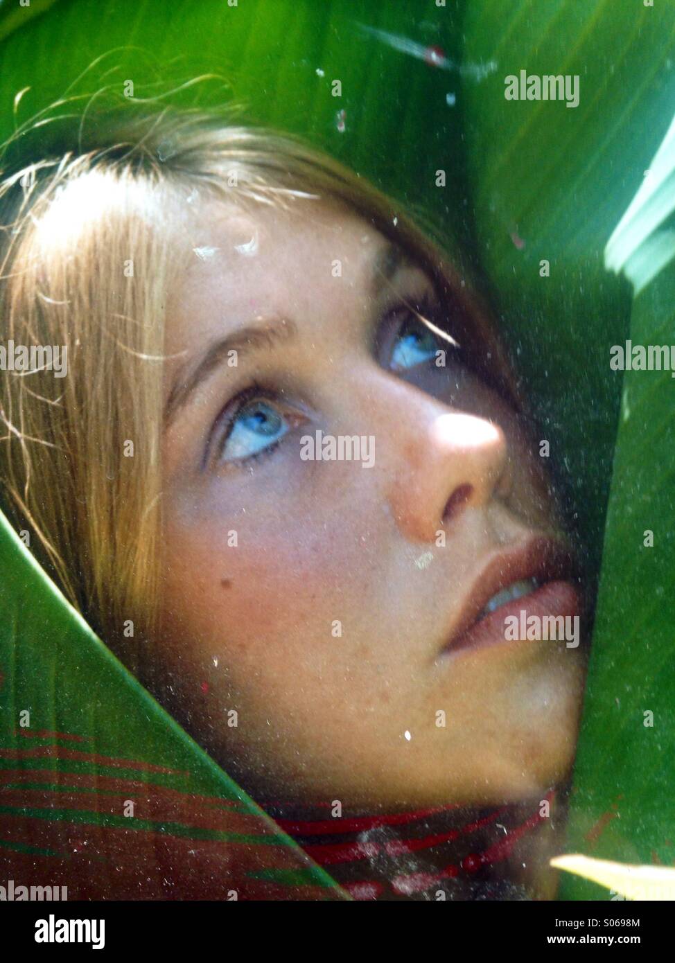 Young woman's face verticale vers le haut à enveloppé dans une feuille de banane verte correspondant à ses yeux. Banque D'Images