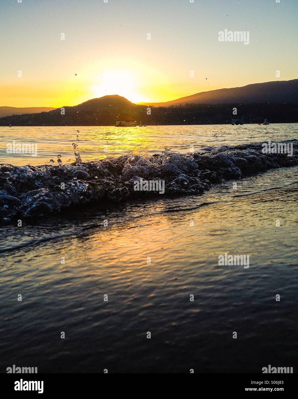 Petites vagues se brisant sur la plage au coucher du soleil ; l'eau de scintillement des bulles et des éclaboussures. Banque D'Images