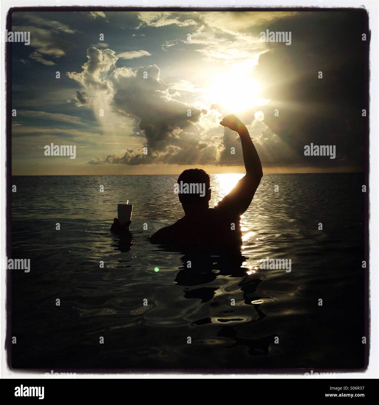 Un homme dans l'eau encourager au coucher du soleil en Floride avec ciel dramatique. Banque D'Images