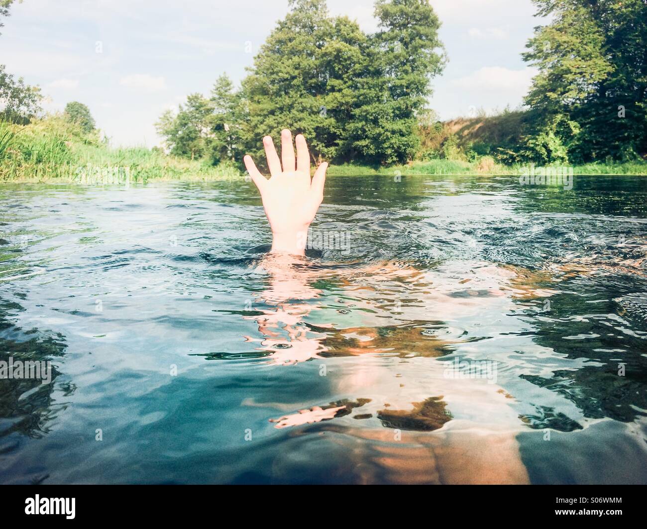 Garçon immergé dans un fleuve en gardant sa main au-dessus de l'eau Banque D'Images
