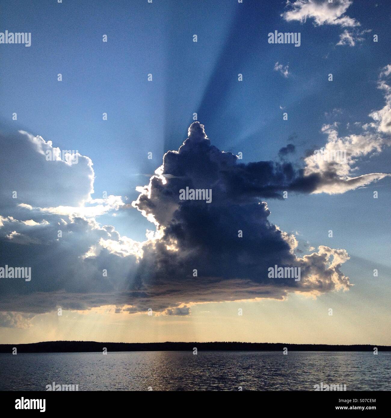 La lumière du soleil spectaculaires effets rayons derrière les nuages au-dessus d'un lac nordique dans le Nord de la Finlande en été - Image de stock capturée avec un smartphone