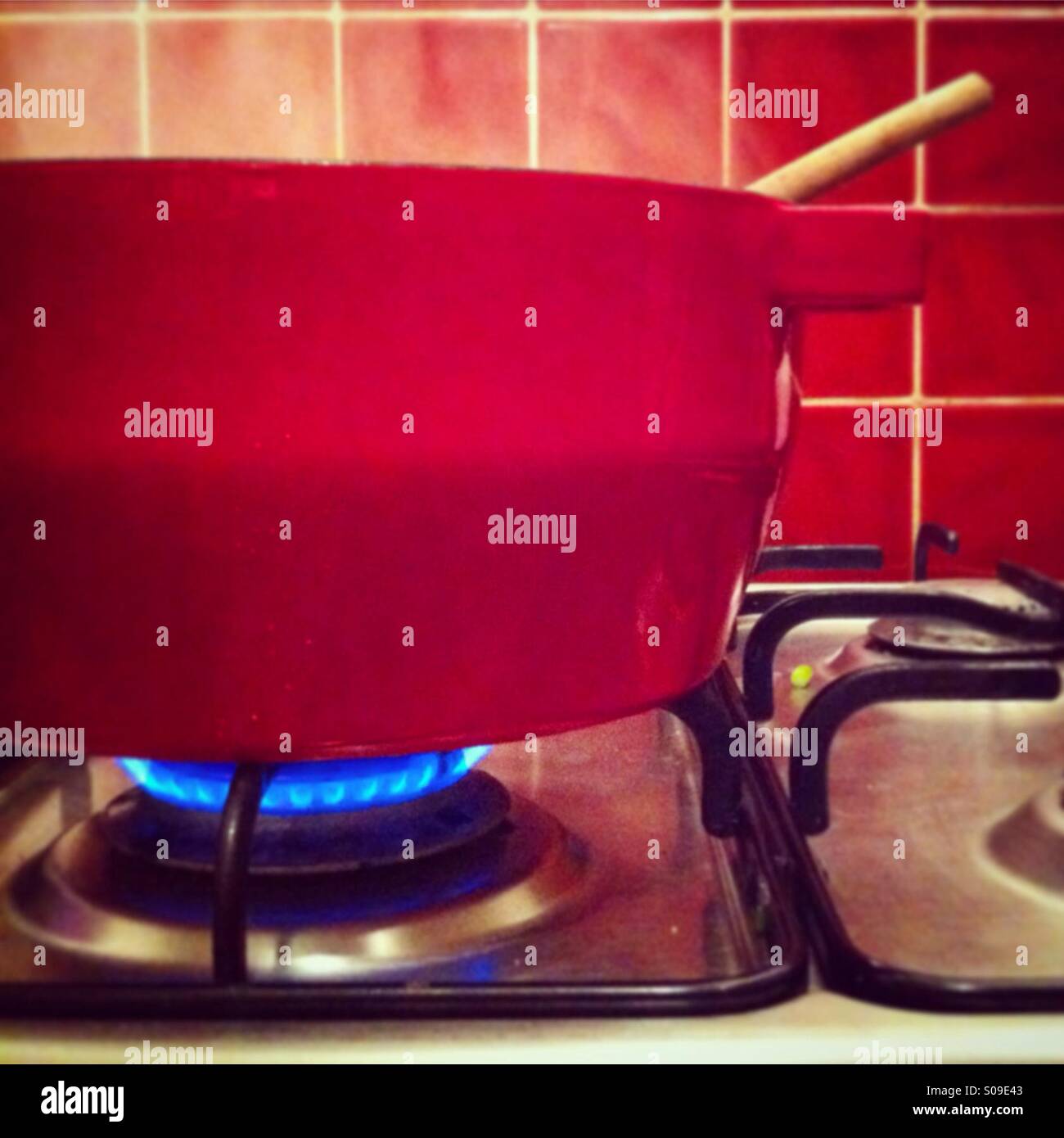 Marmite rouge sur une cuisinière à gaz, de la vapeur à l'intérieur et avec la soupe aux tuiles rouges derrière Banque D'Images