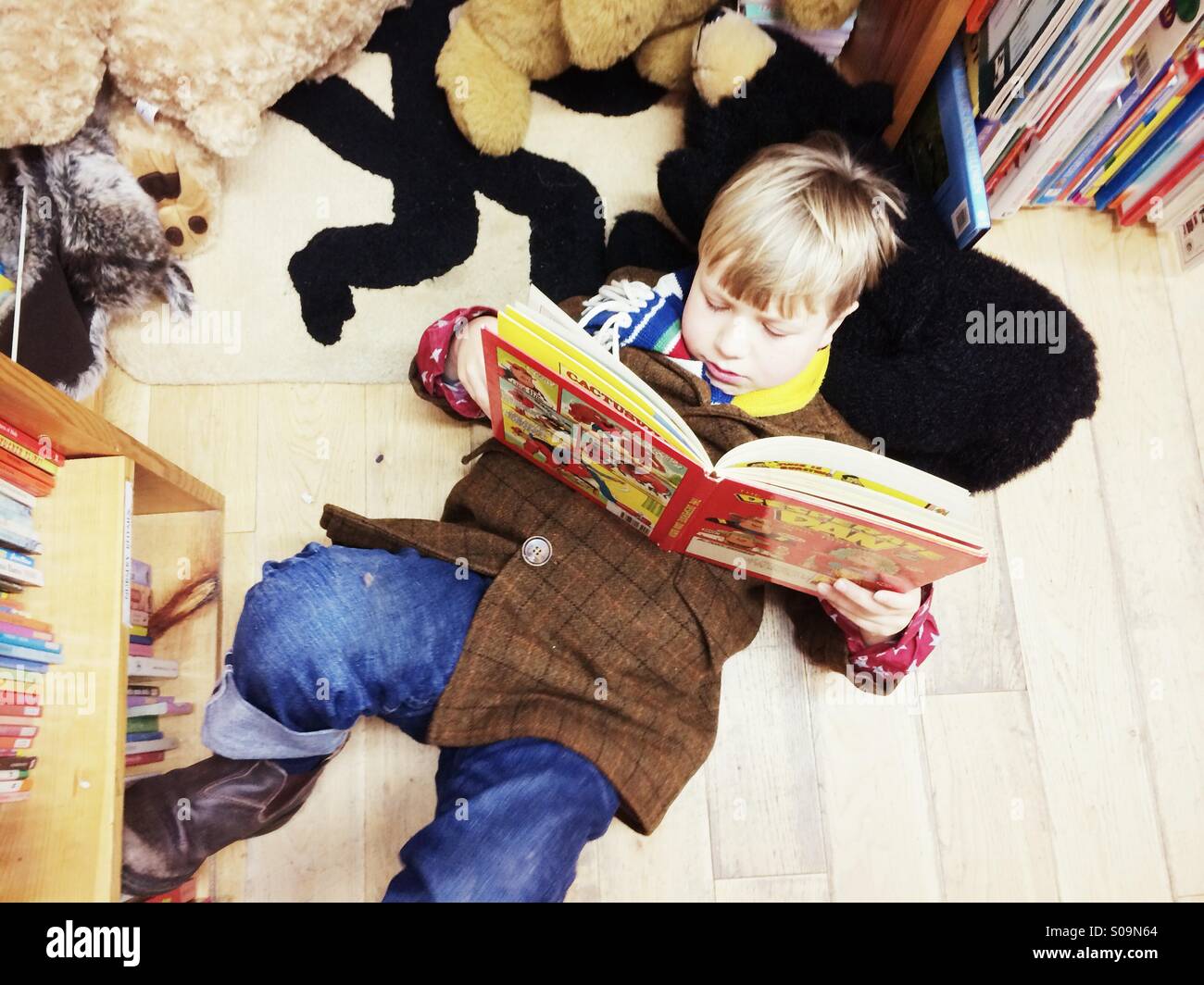 Un jeune garçon à la lecture d'une bande dessinée sur le sol d'une boutique de livres en Angleterre. Banque D'Images