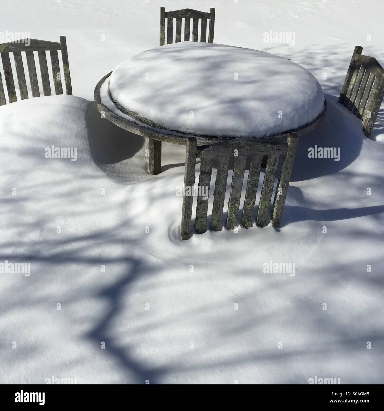 Scène d'hiver de weathered wood table et chaises en bois dans la neige profonde avec des ombres sur la neige Banque D'Images