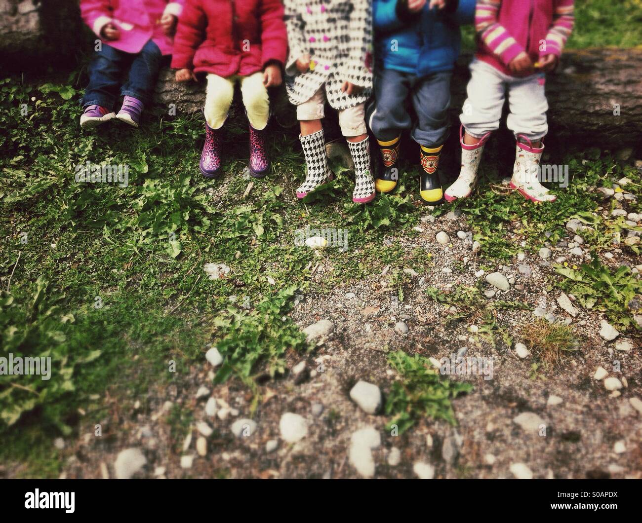 Rangée de jeunes enfants portant des bottes en caoutchouc sur une aire de jeux Banque D'Images