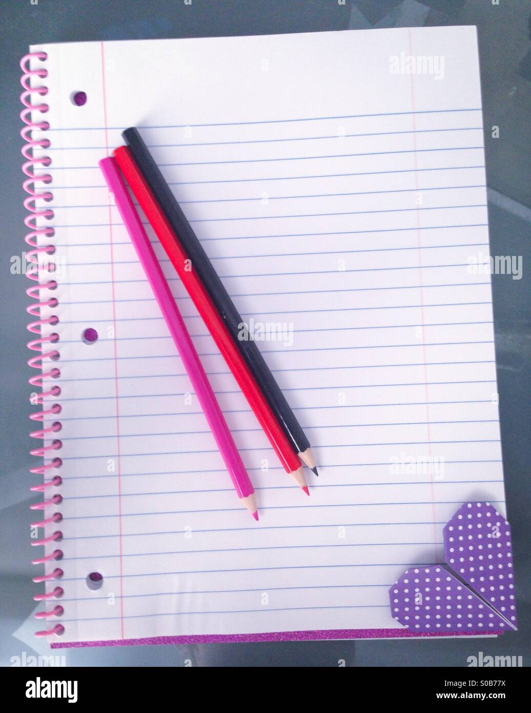 Crayons de couleur et un coeur origami Ajouter aux favoris sur un carnet à spirales. Banque D'Images