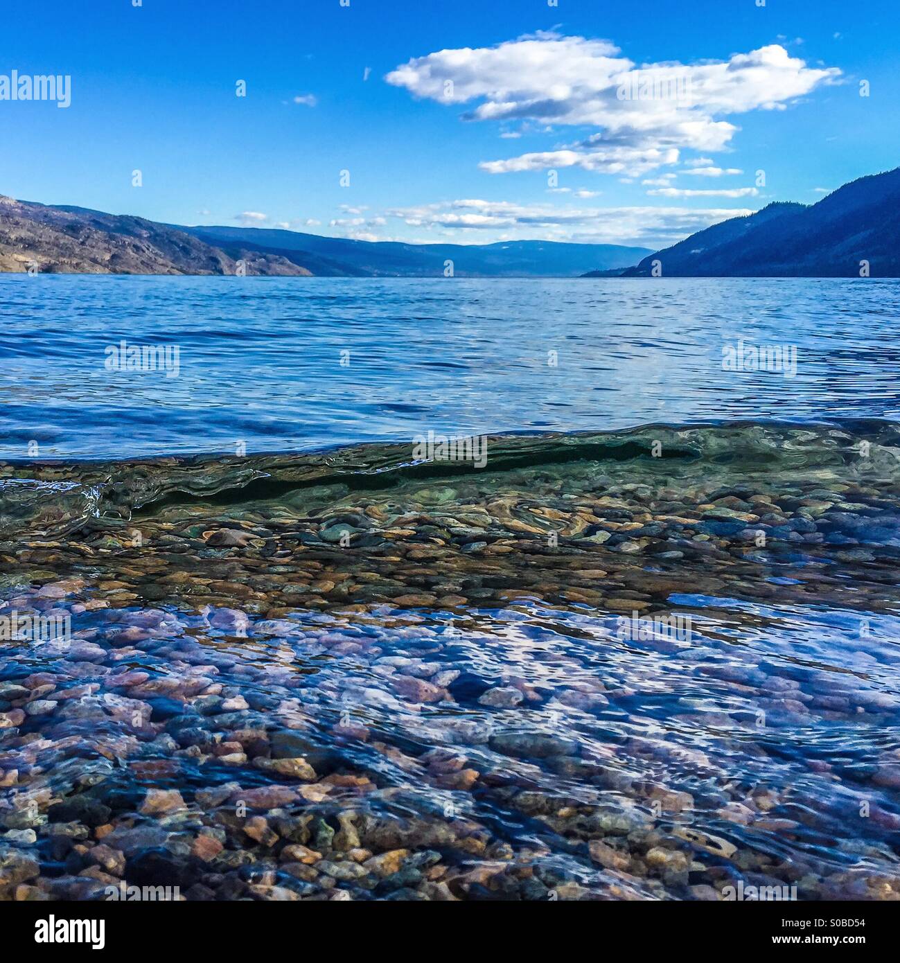 Une petite vague avant de casser les cailloux expose au fond du lac. Banque D'Images