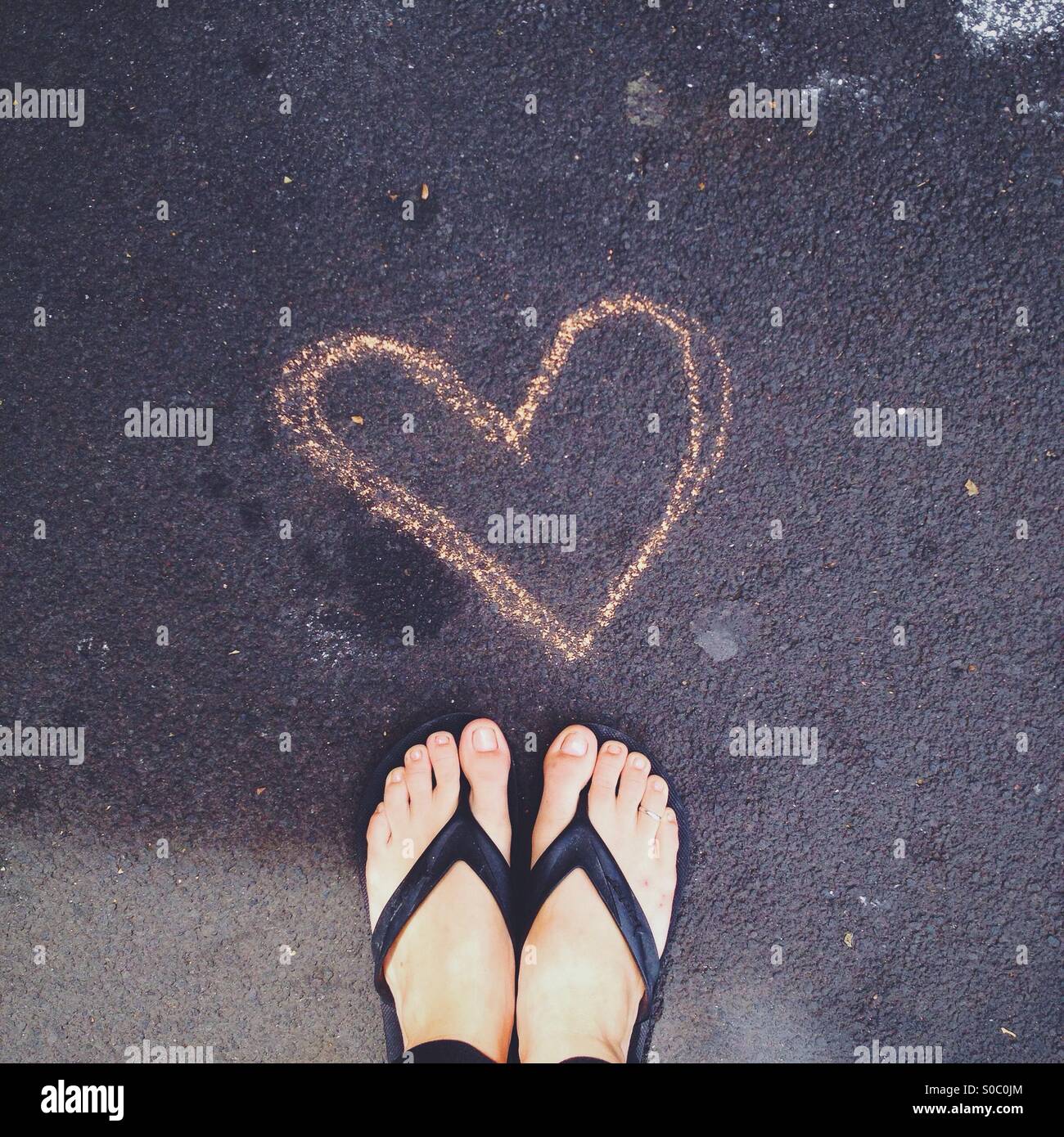 Chalk rose coeur dessiné sur la chaussée avec pieds en sandales Banque D'Images