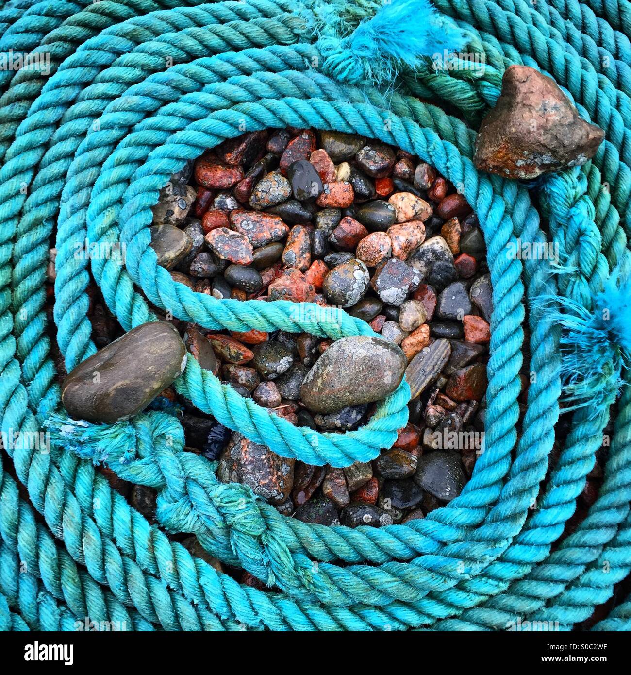 Une bobine de corde bleu bateau sur une plage décrivant la forme d'un neuf et maintenu en position par des pierres et cailloux Banque D'Images