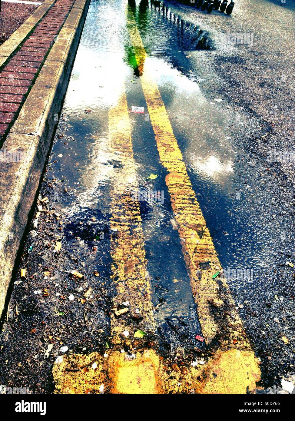Une flaque d'eau contre un trottoir avec double lignes jaunes en passant par elle. - Image de stock capturée avec un smartphone
