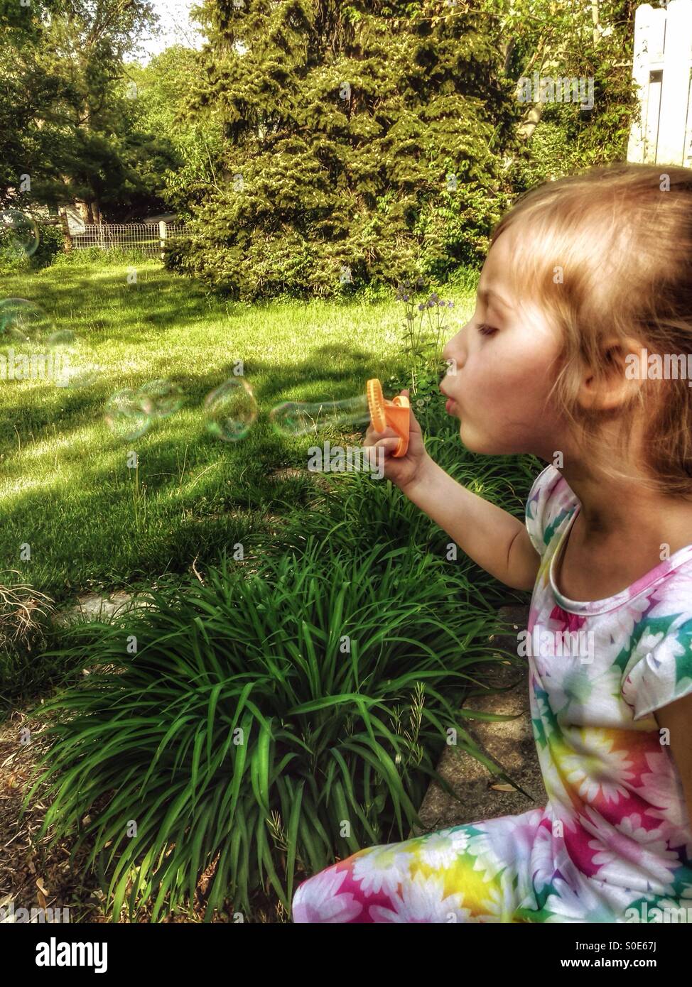 Une fille dans une robe florale est assis sur un patio faisant des bulles (1). Banque D'Images