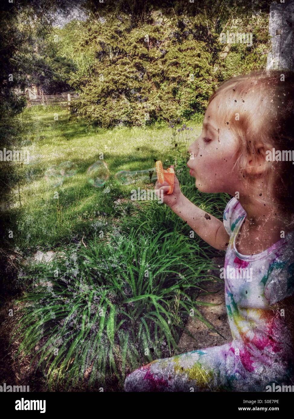 Une fille dans une robe florale est assis sur un patio faisant des bulles (4). Banque D'Images