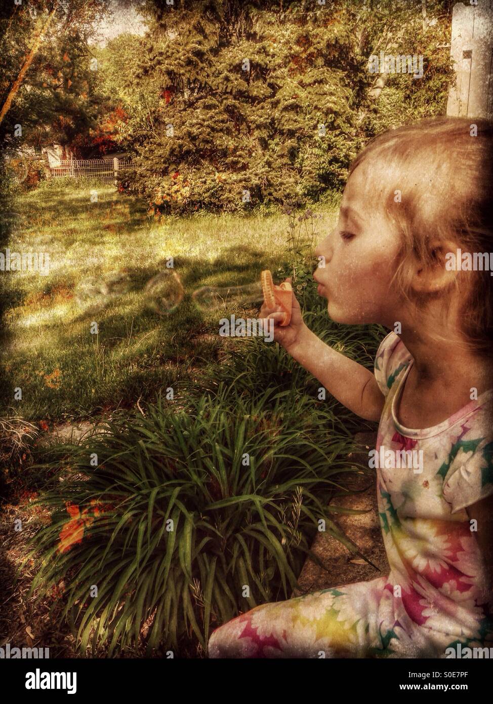 Une fille dans une robe florale est assis sur un patio faisant des bulles (5). Banque D'Images