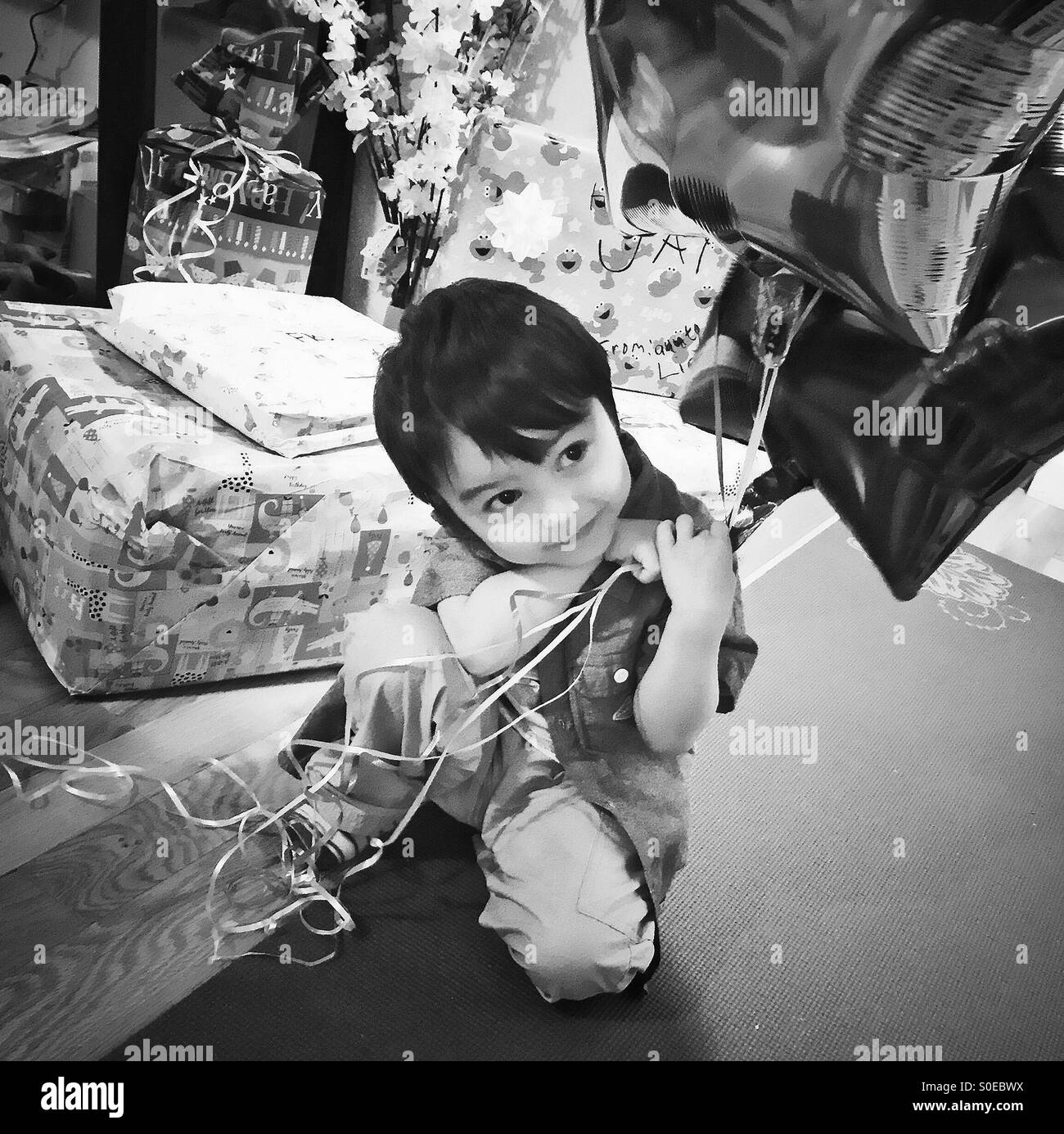 Un petit garçon d'anniversaire pose devant ses dons tout en tenant une grappe de ballons. Banque D'Images