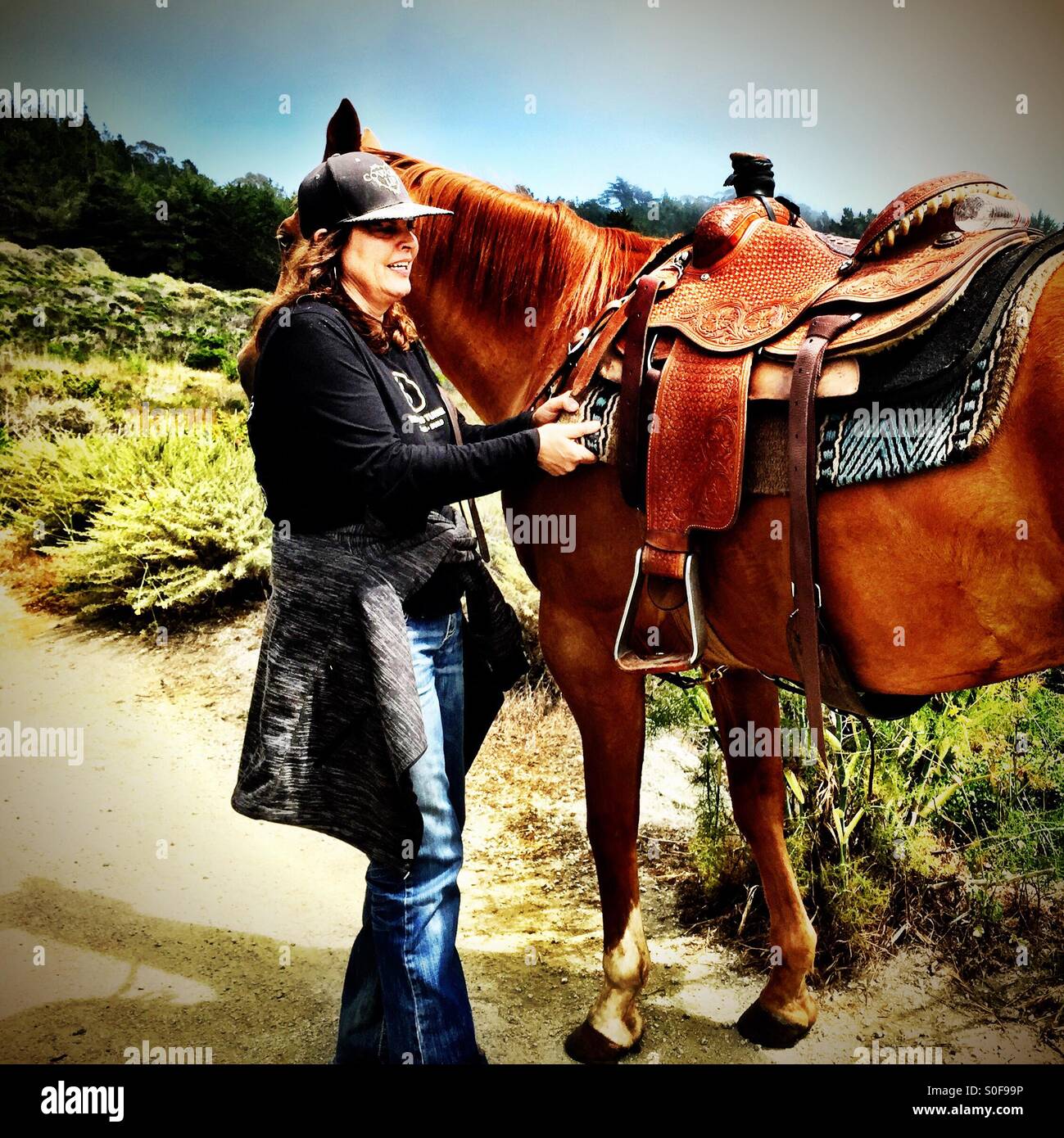 Boucles de fixation de la femme sur son cheval de selle sur un feu de route, McNee Ranch State Park, Californie, USA. - Image de stock capturée avec un smartphone
