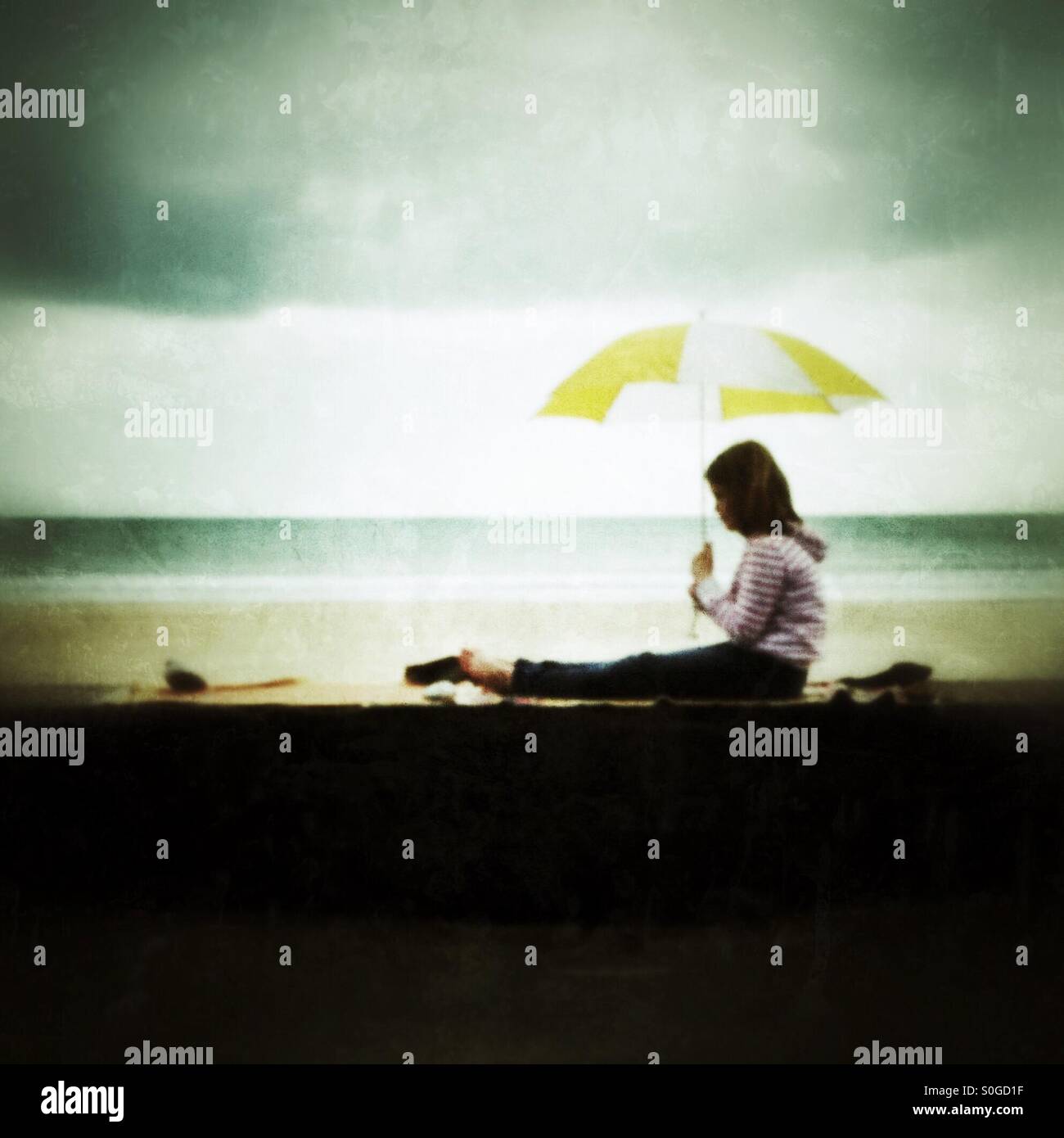 Jeune fille s'assit sur un mur avec un parapluie Banque D'Images