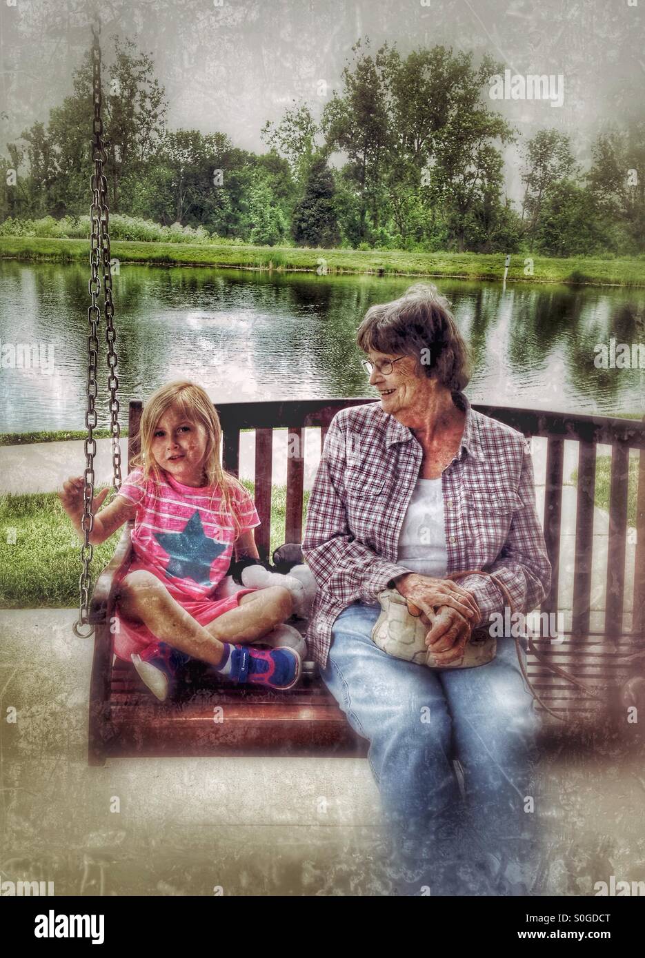 Un enfant assis sur une balançoire avec son arrière grand-mère. Banque D'Images