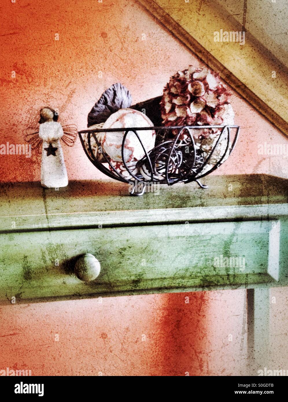 Une table avec un bol de sphères naturelles et un ange du prince par un mur orange (2). Banque D'Images