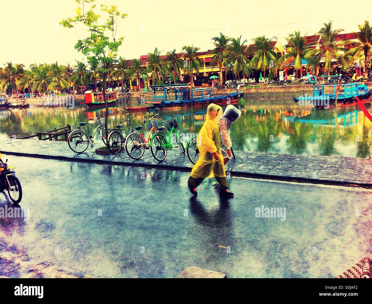 Deux personnes portant des ponchos imperméables à marcher le long du front de mer d'Hoi An, Vietnam - Image de stock capturée avec un smartphone