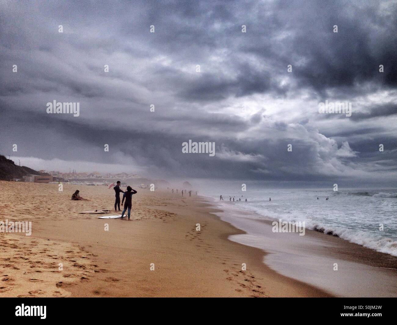 Personnes surfant sous une tempête dans l'océan Atlantique, de la côte ouest du Portugal, avec d'énormes nuages gris et sombre dans le ciel Banque D'Images
