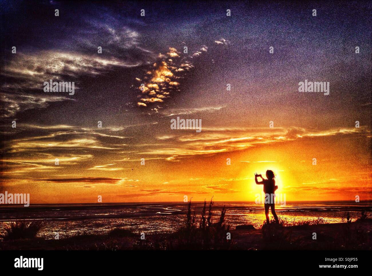 Young Girl taking photo silhouette sur le coucher de soleil sur la baie de Morecambe Heysham au Banque D'Images