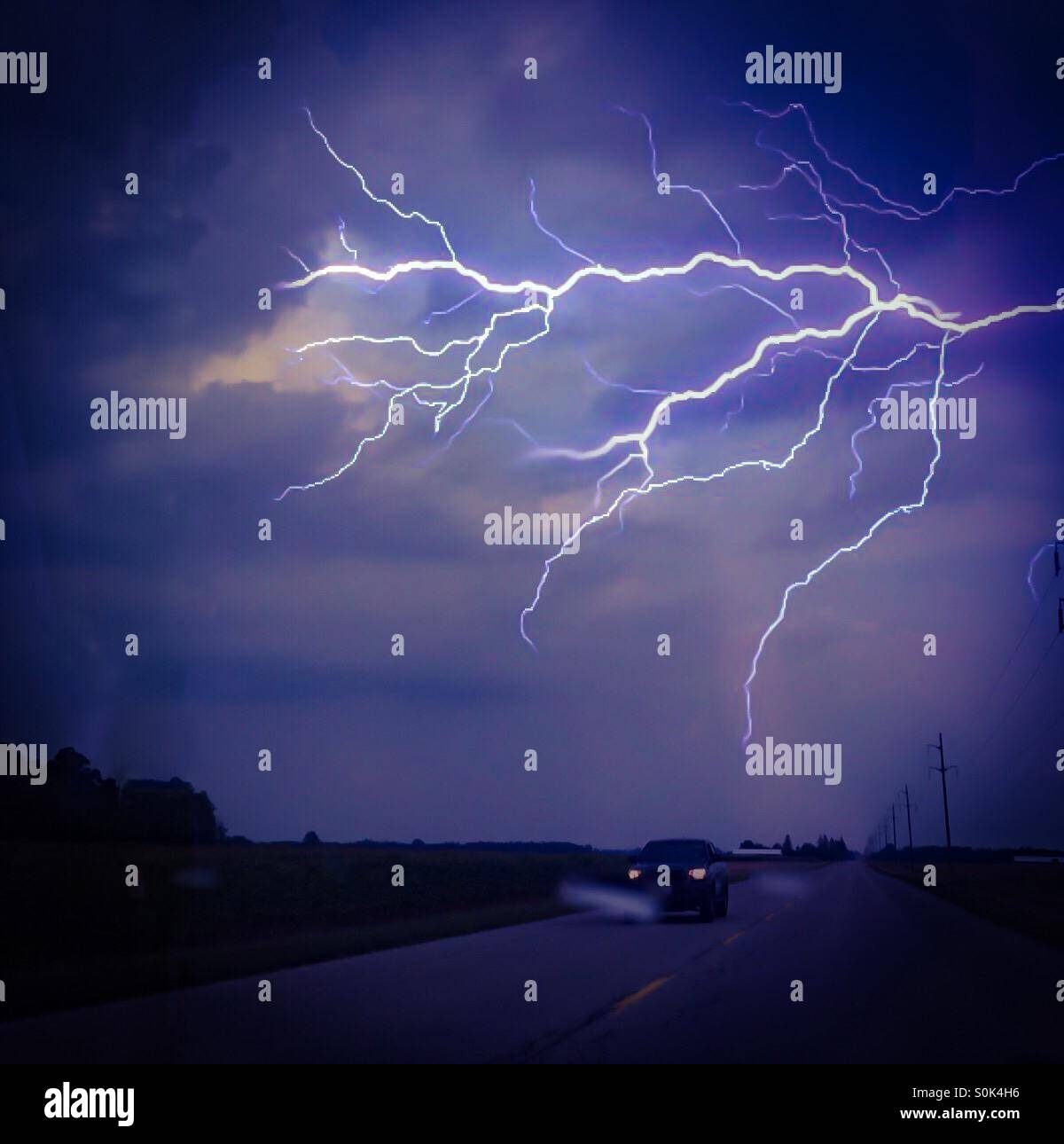 Une nuit de tempête. Un éclair éblouissant illumine un ciel sombre. Circulation légère sur la route ci-dessous. Concepts : nature, puissance, stupeur. Au-delà de l'humain. - Image de stock capturée avec un smartphone