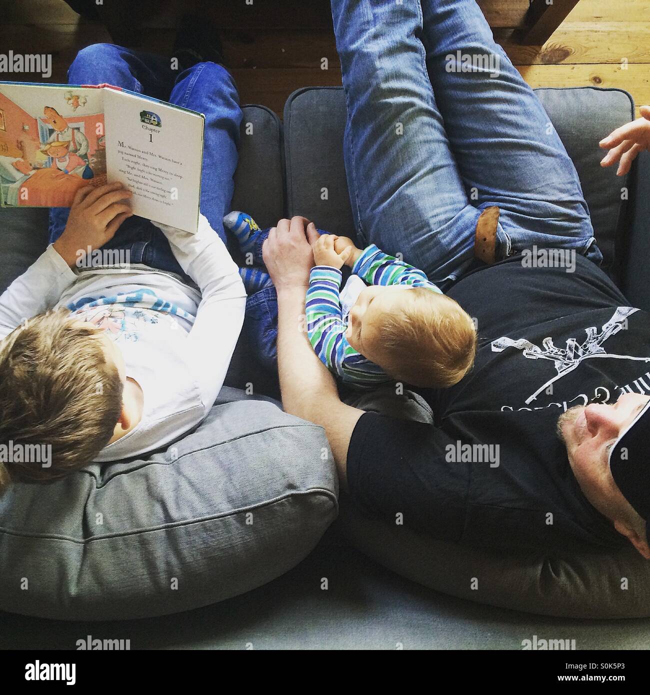 À partir de la photo ci-dessus) d'un père avec ses deux enfants , sur de qui est en train de lire un livre à haute voix à son jeune frère , assis sur un canapé gris. Banque D'Images