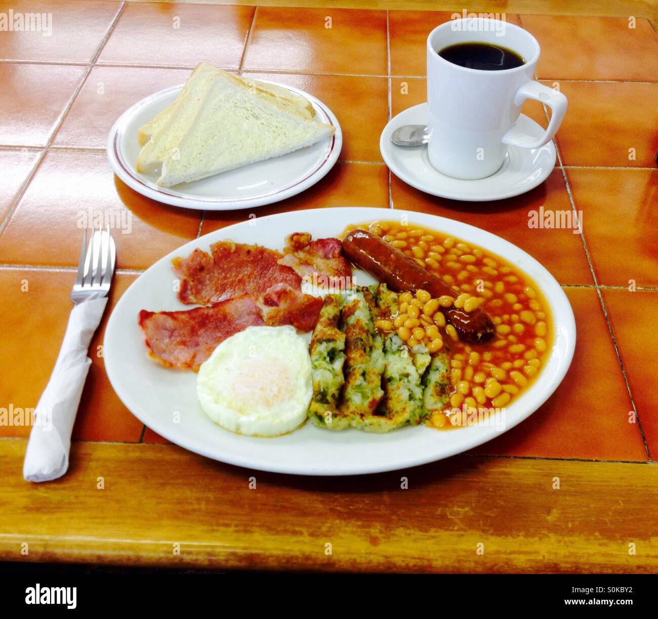 Petit-déjeuner anglais complet avec du bacon frit oeufs saucisse haricots et mug de café noir Banque D'Images