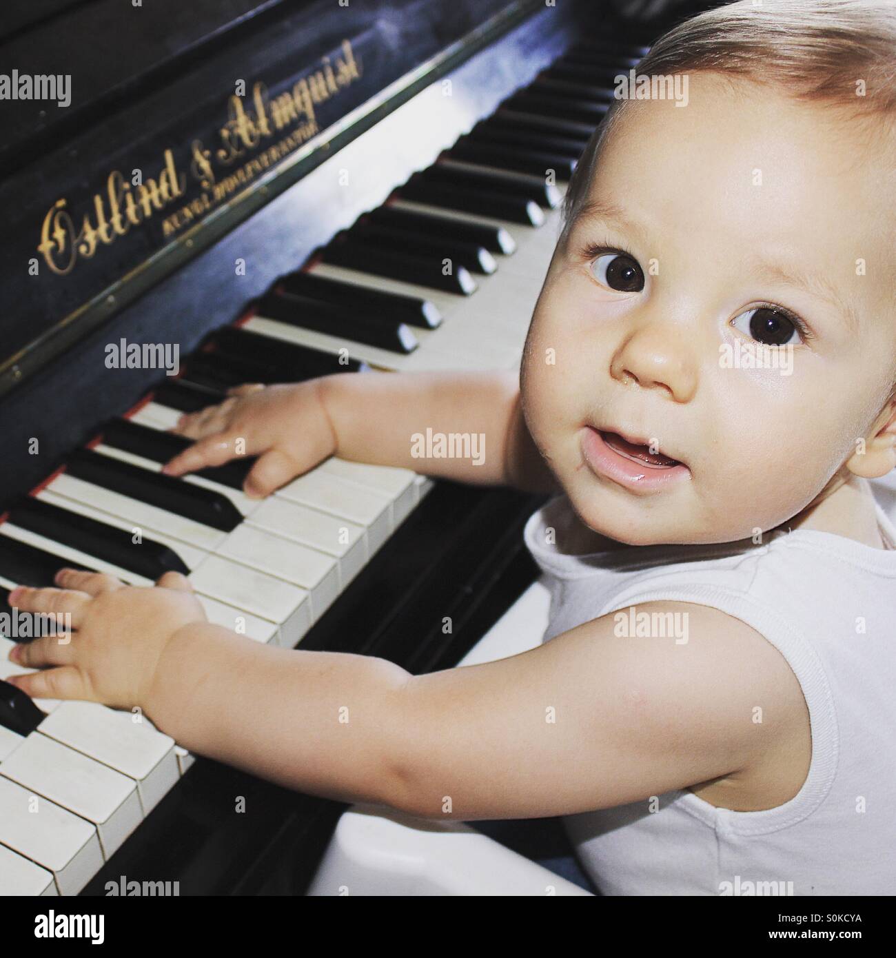 9 mois bébé garçon jouant du piano , avec ses deux mains sur le clavier du piano, regardant la caméra avec une expression de joie sur son visage Banque D'Images