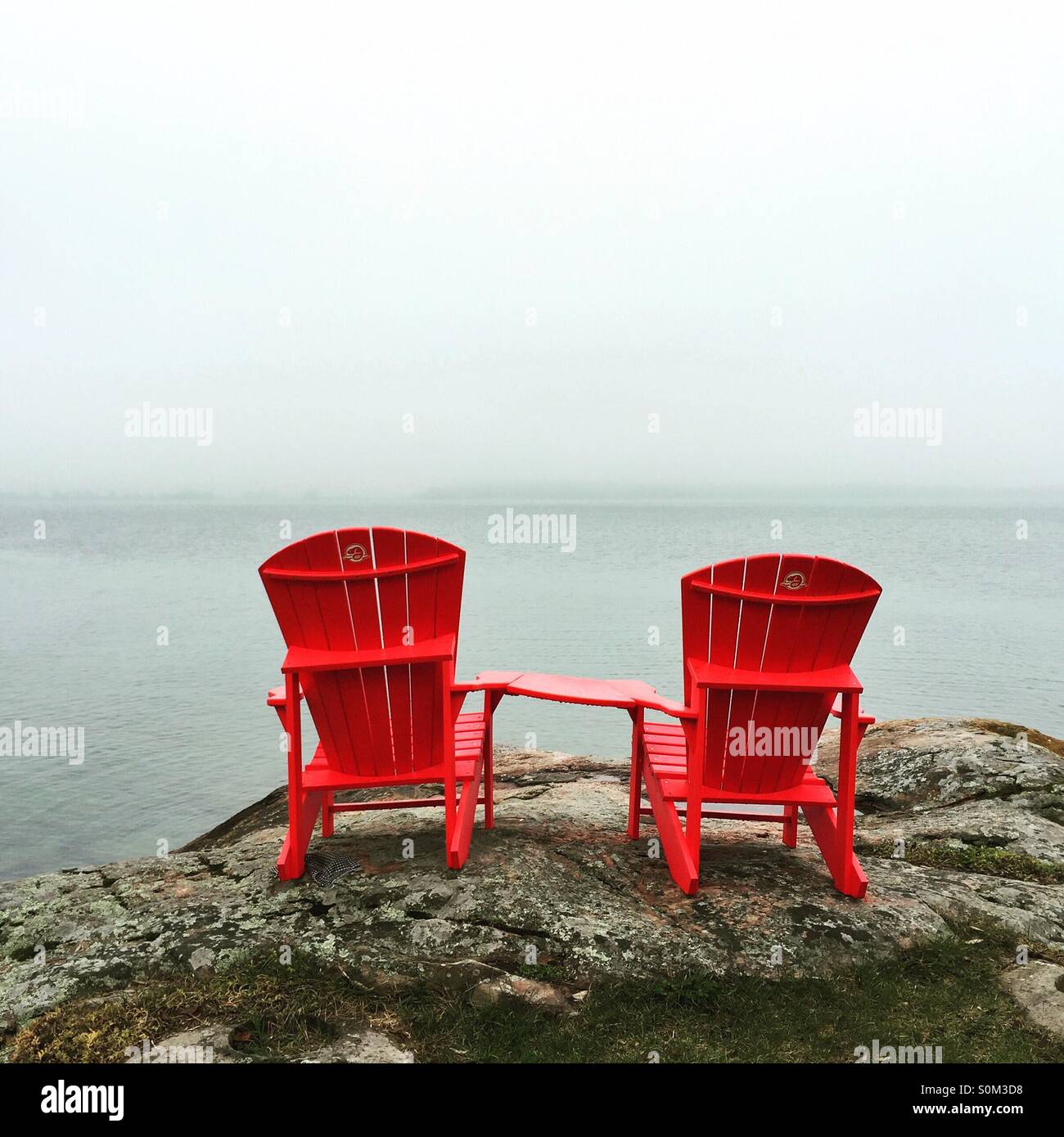 Seuls deux chaises rouges qui domine le fleuve Saint-Laurent sur un jour brumeux, nuageux Banque D'Images